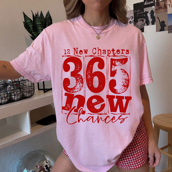 Distressed 12 New Chapters, 365 New Chances RED DTF Heat Transfer - Close-up of a pink t-shirt with bold red distressed print of the words '12 New Chapters, 365 New Chances' in various fonts and styles.