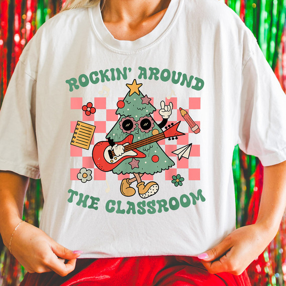 Rockin' Around The Classroom DTF Heat Transfer, festive Christmas-themed graphic of a cute Christmas tree character playing guitar with accessories like a paper airplane, notebook, and crayons on a classroom background.