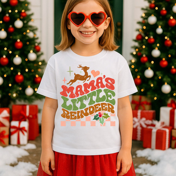 Distressed Mama's Little Reindeer Peach DTF Heat Transfer, festive holiday girl wearing Christmas-themed t-shirt with reindeer and holiday message, surrounded by decorated Christmas trees and presents.