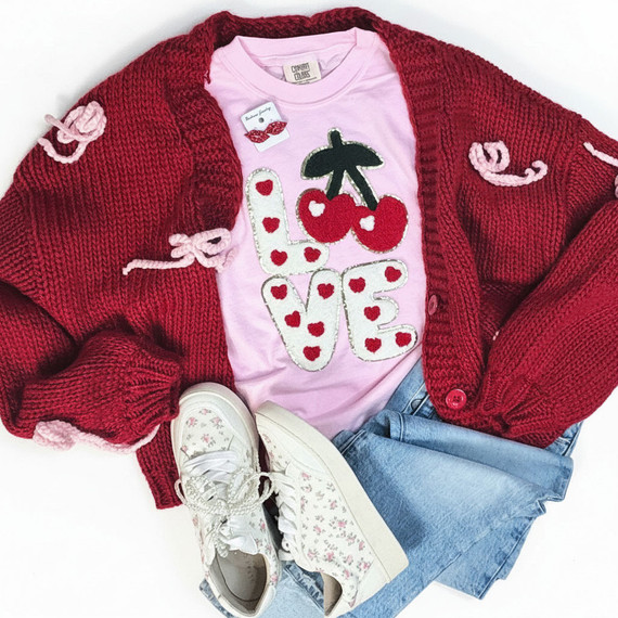Love with Cherries Chenille Patch, pink t-shirt with cherry and heart love design, paired with red knitted cardigan with pink bows, floral sneakers, and blue jeans.