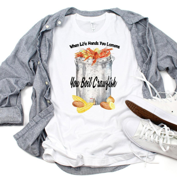 When Life Hands You Lemons Boil Crawfish sublimation transfer on a white T-shirt with seafood graphics, surrounded by a gray shirt and white shoes.