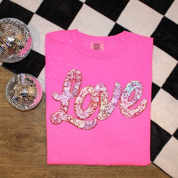 Faux Sequin Love Script DTF Heat Transfer, pink t-shirt with love text made of pink sequins, flat lay on checkered and wooden background.
