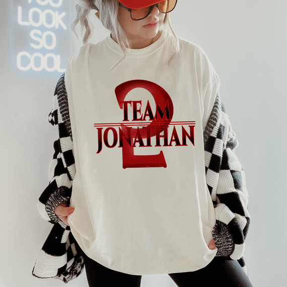 Team Jonathan ST DTF Heat Transfer, a red and black graphic design on a white T-shirt worn by a woman with glasses, gray hair, and a black and white checkered sweater.