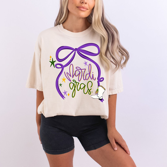 Mardi Gras Oversized Bow DTF Heat Transfer, colorful Mardi Gras themed design with a purple bow, star and shoe graphics on a woman's t-shirt.