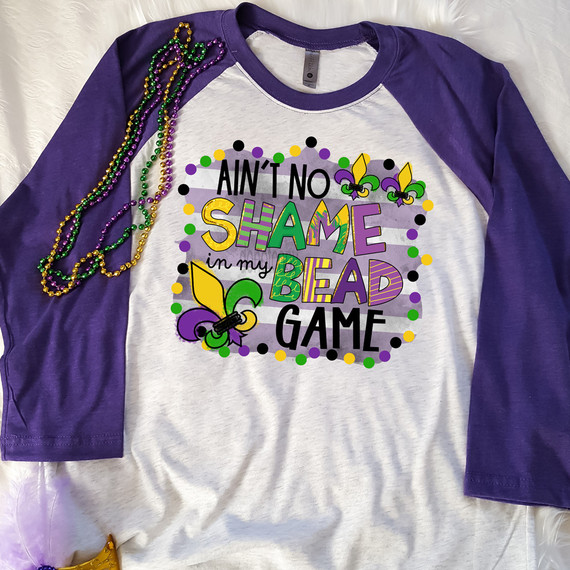 Ain't No Shame In My Bead Game DTF Heat Transfer, colorful Mardi Gras themed t-shirt with beads and decorative beads on the shoulder.