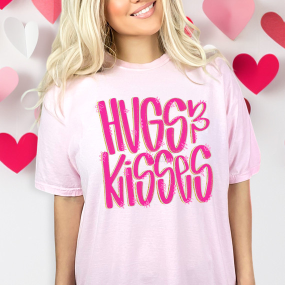 Hugs & Kisses DTF Heat Transfer, pink and gold design on a light pink t-shirt with heart decorations in the background.