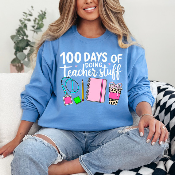 100 Days Of Doing Teacher Stuff DTF Heat Transfer, a woman wearing a blue sweatshirt with a colorful design and text related to teachers and school supplies.