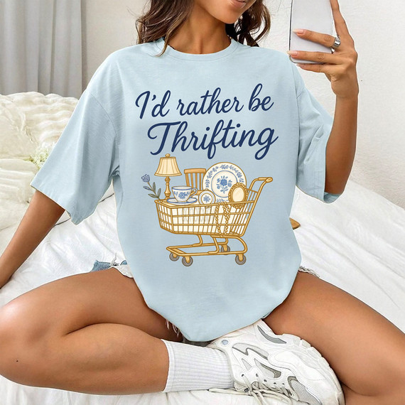 I'd Rather Be Thrifting Vintage Cart DTF Heat Transfer, a woman wearing a light blue oversized T-shirt with a decorative shopping cart filled with vintage items and the text 'I'd rather be Thrifting' in stylish font.