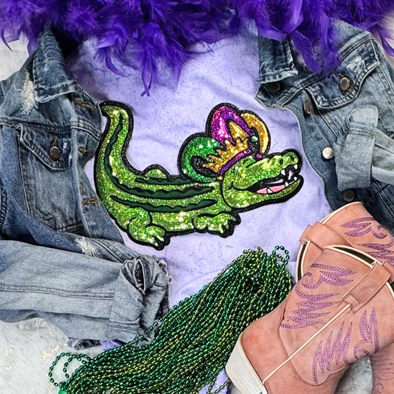 Mardi Gras Gator Sequins Patch, colorful sparkling green, purple, and yellow embroidered patch on a purple shirt, surrounded by denim jacket, pink cowboy boot, and green beads.