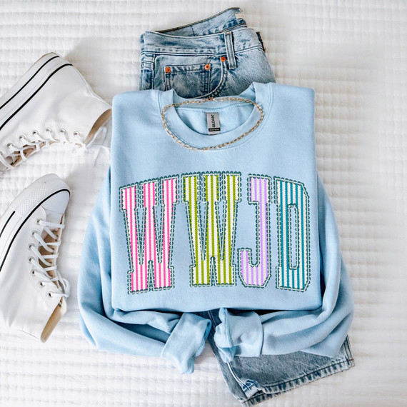 WWJD Seersucker DTF Heat Transfer, a colorful embroidered design on a light blue sweatshirt.