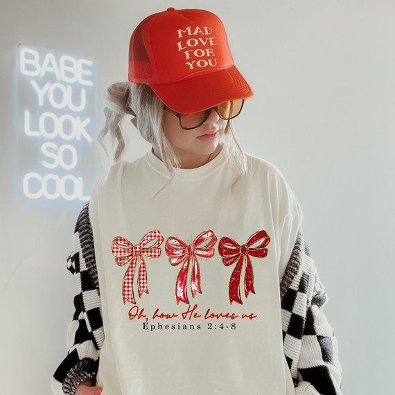 Oh How He Loves Us Bow Trio BLACK DTF Heat Transfer, red trucker cap with 'MAD LOVE FOR YOU' text, and graphic t-shirt with three red bows and Bible verse from Ephesians 2:4-8.