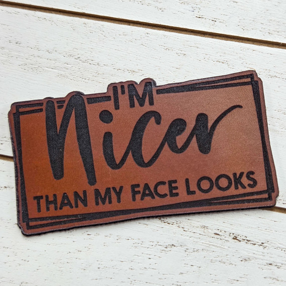 I'm Nicer Than My Face Looks Leather Hat Patch, brown leather patch with black text and border showcasing humorous quote.