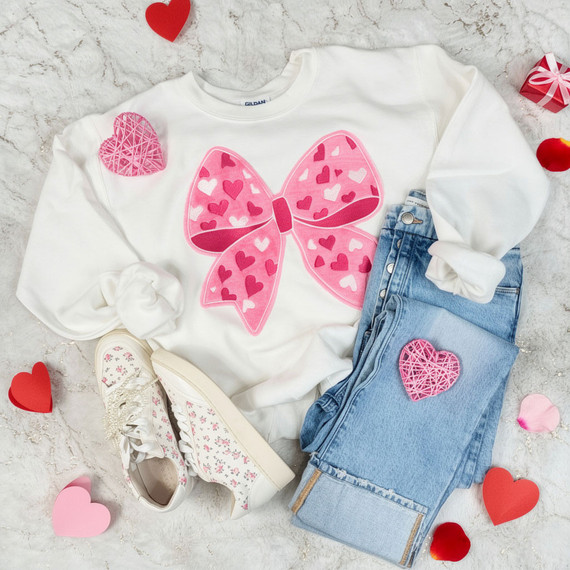 Fluffy Heart Bow Patch – Soft Textured Velvet, pink bow patch with heart pattern on a white sweatshirt, placed alongside blue jeans with a matching pink heart patch, and floral sneakers, surrounded by red, pink, and white heart-shaped decorations.