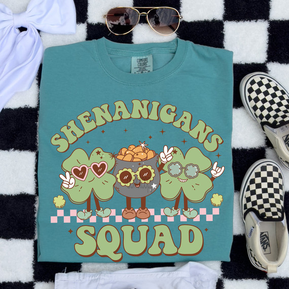 Retro Shenanigans Squad DTF Heat Transfer, cartoon-style graphic of three cheerful shamrocks with sunglasses, peace signs, and a pot of gold, on a teal T-shirt with playful text and design elements.