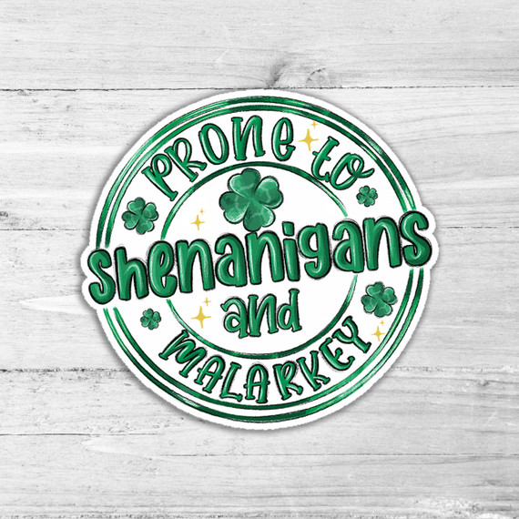 Prone To Shenanigans Die Cut Sticker, festive green shamrocks and gold stars with playful text on a white wooden background.