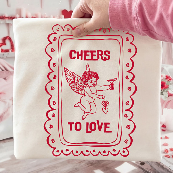 Cheers To Love Cupid DTF Heat Transfer, red outline design of Cupid with wings, holding a cocktail and a four-leaf clover, surrounded by hearts and decorative border.