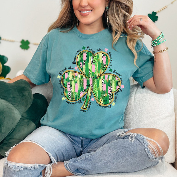 Blessed Vibes Brushstroke Shamrock DTF Heat Transfer, colorful shamrock design with brushstroke patterns and around text saying 'Blessed vibes' on a turquoise t-shirt.