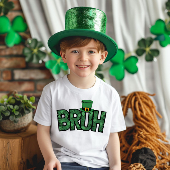 Bruh St Patricks Day DTF Heat Transfer, a boy wearing a white t-shirt with a green shamrock-shaped graphic and a leprechaun hat, celebrating St. Patrick's Day with festive decorations in the background.