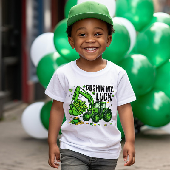 Pushin' My Luck Excavator DTF Heat Transfer, a vibrant green-colored excavator graphic with four-leaf clovers, on a white T-shirt worn by a smiling boy in front of green and white balloons.