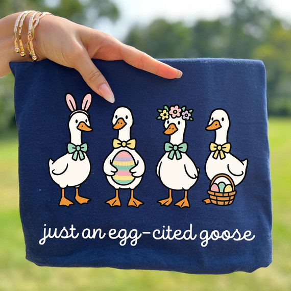 Just an Egg-Cited Goose DTF Heat Transfer, decorative design featuring four cartoon geese with Easter accessories and the phrase 'just an egg-cited goose' on a navy blue fabric background.