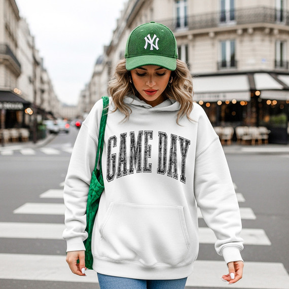 Distressed Game Day BLACK DTF Heat Transfer, a black heat transfer design shown on a white hoodie worn by a woman in an urban street setting.