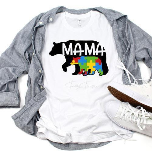 Autism Awareness Mama Bear Sublimation Transfer, T-shirt with a bear graphic filled with colorful puzzle pieces and the word 'MAMA' in black, laid on a gray shirt and sneakers.
