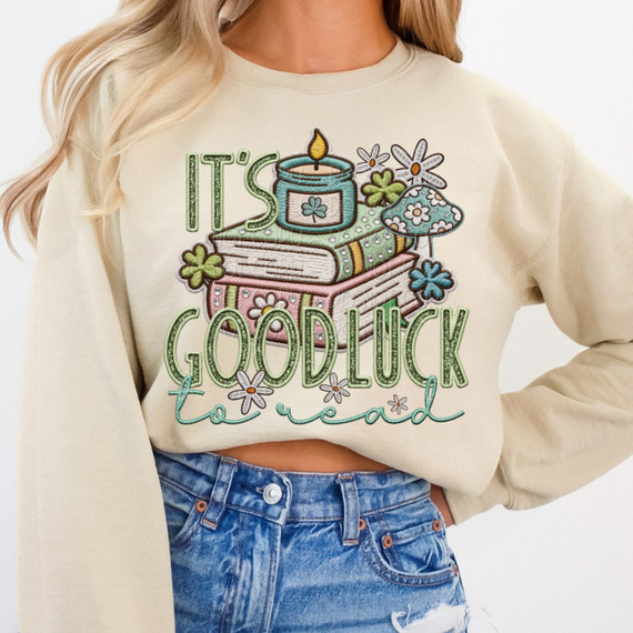 It's Good Luck To Read DTF Heat Transfer, colorful embroidered design on a beige sweatshirt featuring books, flowers, a candle, and decorative text.