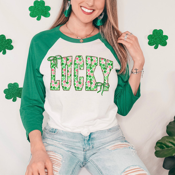 Shamrock Lucky Bow DTF Heat Transfer, close-up of a woman wearing a St. Patrick's Day themed shirt with shamrocks and the word 'Lucky' decorated with shamrocks and bows, festive green accessories, and surrounded by shamrock wall decorations.