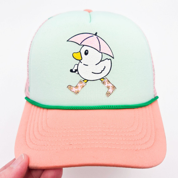 Glitter Duck Hat/Pocket Screen Print Heat Transfer, pastel-colored baseball cap with a duck holding a pink umbrella and wearing floral boots embroidered on the front panel.