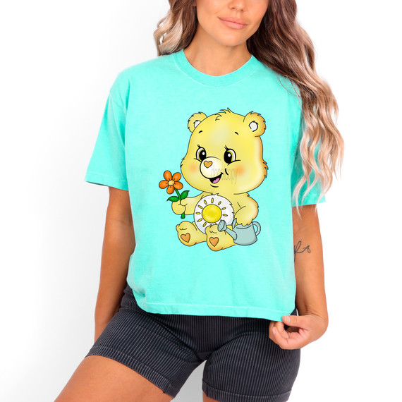 Sunny Bear DTF Heat Transfer, colorful bear cartoon holding a flower and watering can on a turquoise t-shirt.