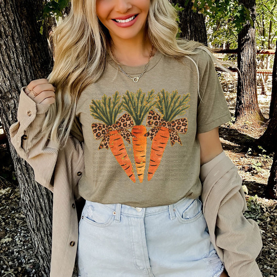 Faux Glitter Leopard Bow Carrots DTF Heat Transfer, a girl wearing a t-shirt with a decorative carrot design featuring green tops, orange carrots with glitter and leopard print bows, in a forest setting.