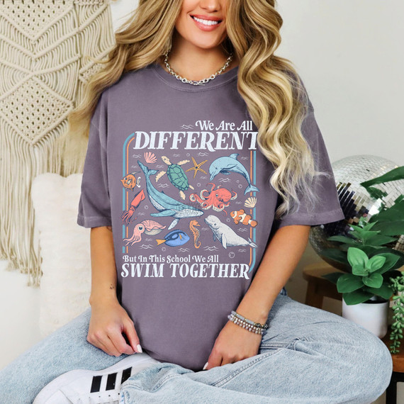 We Are All Different Ocean DTF Heat Transfer, colorful aquatic-themed design featuring various sea creatures and the message 'We Are All Different But In This School We All Swim Together' on a purple t-shirt.