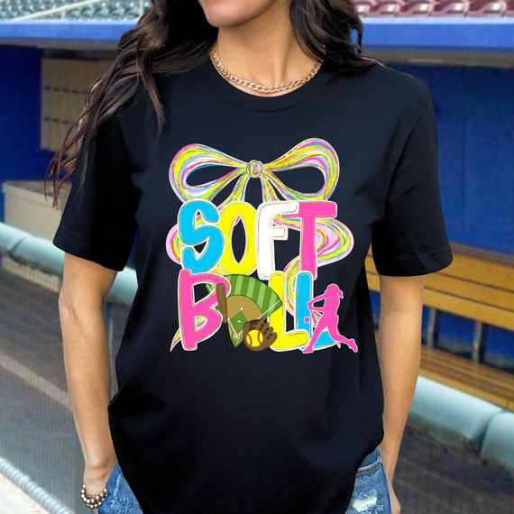 Softball Oversized Bow DTF Heat Transfer - Colorful design with a large bow and multiple sports-related icons on a black T-shirt worn by a woman outdoors.