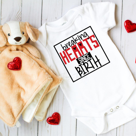 Breaking Hearts Since Birth Valentine Black Text Sublimation Transfer on baby onesie, worn next to a plush teddy bear and surrounded by red hearts.