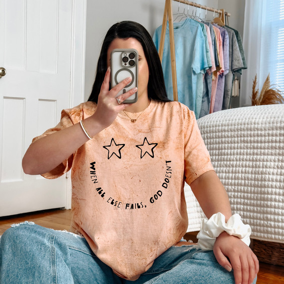 When All Else Fails God Doesn't DTF Heat Transfer, a woman taking a mirror selfie in a cozy room with a peach-colored t-shirt featuring the slogan and star design.