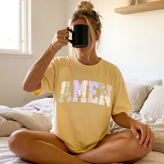 Faux Fabric Patchwork Amen DTF Heat Transfer, woman sitting cross-legged on bed holding a black mug with a yellow T-shirt with patchwork letter design.