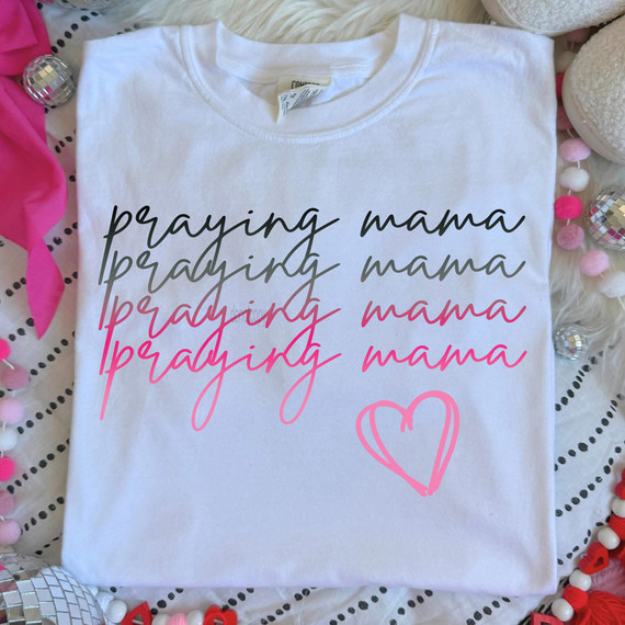Praying Mama Stacked DTF Heat Transfer, white T-shirt with layered handwritten style 'praying mama' text in black, gray, and pink, along with a pink heart illustration.