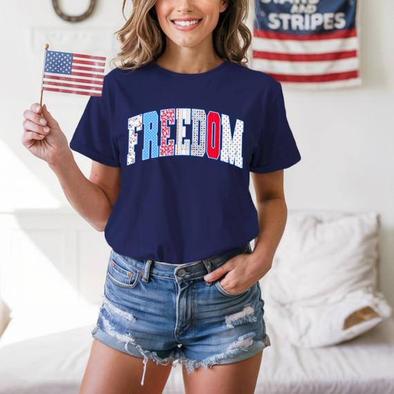 Freedom Patchwork DTF Heat Transfer, woman holding small American flag and wearing a patriotic T-shirt with 'FREEDOM' text in red, white, and blue.