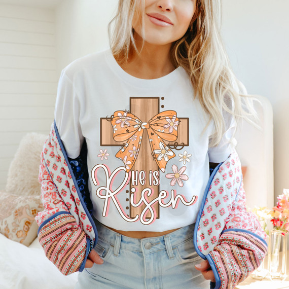 He Is Risen DTF Heat Transfer, colorful religious design featuring a cross with a bow and floral accents on a woman wearing a white t-shirt.