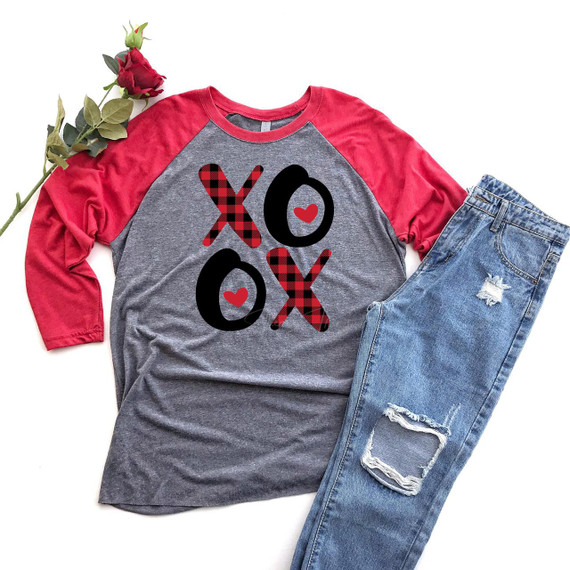 Valentine Plaid XOXO Screen Print Heat Transfer, a graphic of the word 'XOXO' with hearts and red and black plaid design, printed on a casual raglan t-shirt with jeans and a red rose.