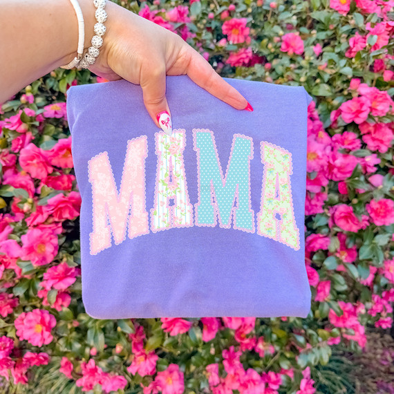 Cottagecore Patterned Mama DTF Heat Transfer, colorful fabric with the word MAMA in pastel patterned letters held against pink flowering bushes