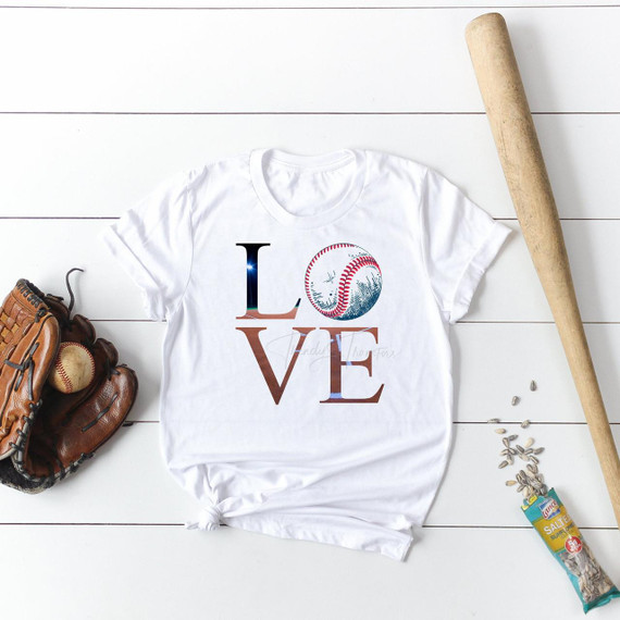 Love Baseball Sublimation Transfer-1655971499, white T-shirt with a baseball graphic and the word 'LOVE' printed on it, surrounded by baseball glove, ball, bat, and sunflower seeds on a white wooden surface.