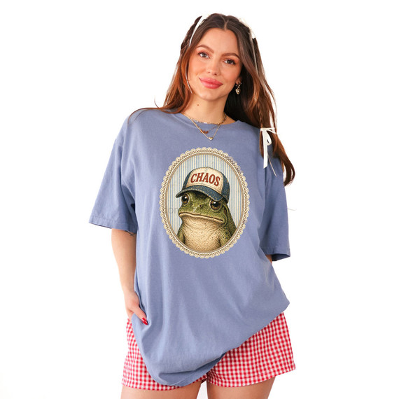 Chaos Frog DTF Heat Transfer, a woman modeling a blue t-shirt with a frog wearing a cap that says 'CHAOS' inside a decorative oval frame.