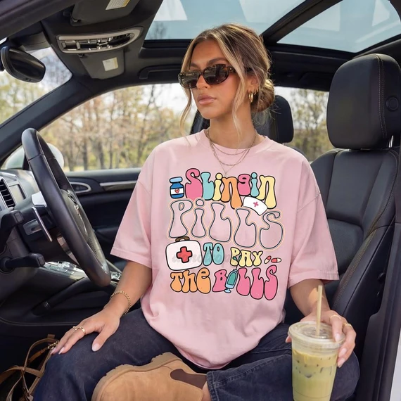 Slingin' Pills To Pay The Bills DTF Heat Transfer, young woman sitting in car holding iced drink, wearing pink T-shirt with medicine themed graphic design.