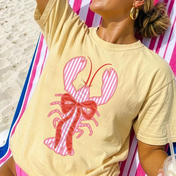 Seersucker Lobster DTF Heat Transfer, colorful lobster with bow design on a woman's yellow t-shirt at the beach.