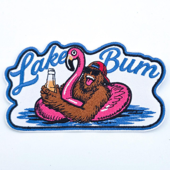 Lake Bump Bigfoot Oversized Embroidered Hat Patch – 5 Inch Wide Statement Design, featuring a colorful embroidery of a bearded man with sunglasses and a backward cap lounging on a pink flamingo float and holding a drink, with the text 'Lake Bum' in blue cursive.