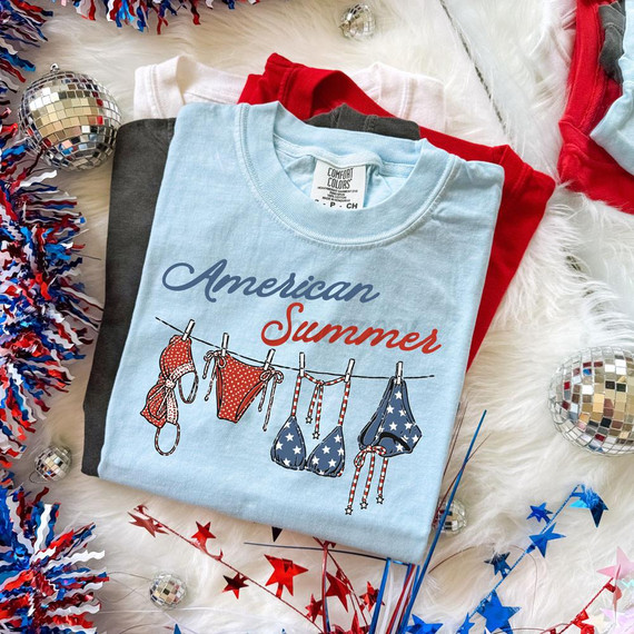 American Summer Patriotic Bikini DTF Heat Transfer, folded patriotic bikini T-shirt with American flag-themed bikini illustration and text, surrounded by patriotic decorations on a festive background.