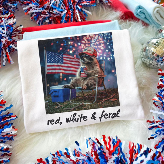 Red, White & Feral BLACK DTF Heat Transfer, featuring a raccoon wearing a patriotic hat and sunglasses, holding a drink with an American flag background and fireworks.