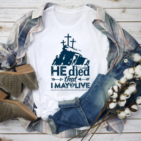Easter He Died That I May Live Sublimation Transfer, product t-shirt with religious design featuring crosses and a hill, placed on a flat lay with shoes, jeans, plaid shirt, and cotton branches.