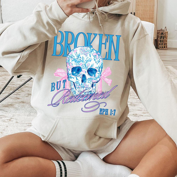 Broken But Redeemed Skull DTF Heat Transfer, colorful skull design with floral patterns and pink ribbons on a beige hoodie.